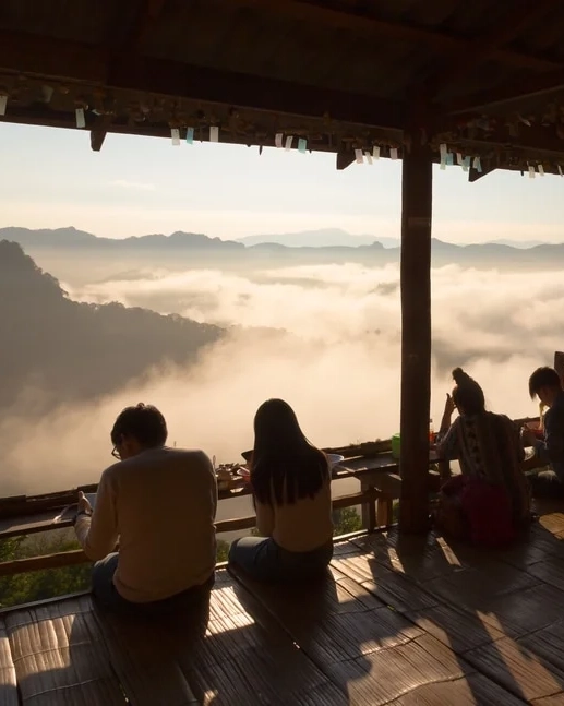 People sitting at a wooden bench eating noodles at the elevated Ban Ja Bo Village in Thailand, with a sea of clouds at their feet. Image credit: Shutterstock