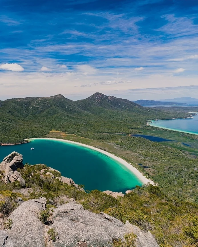 Two people look over a stunning view of Wineglass Bay and the peninsula at Freycinet.