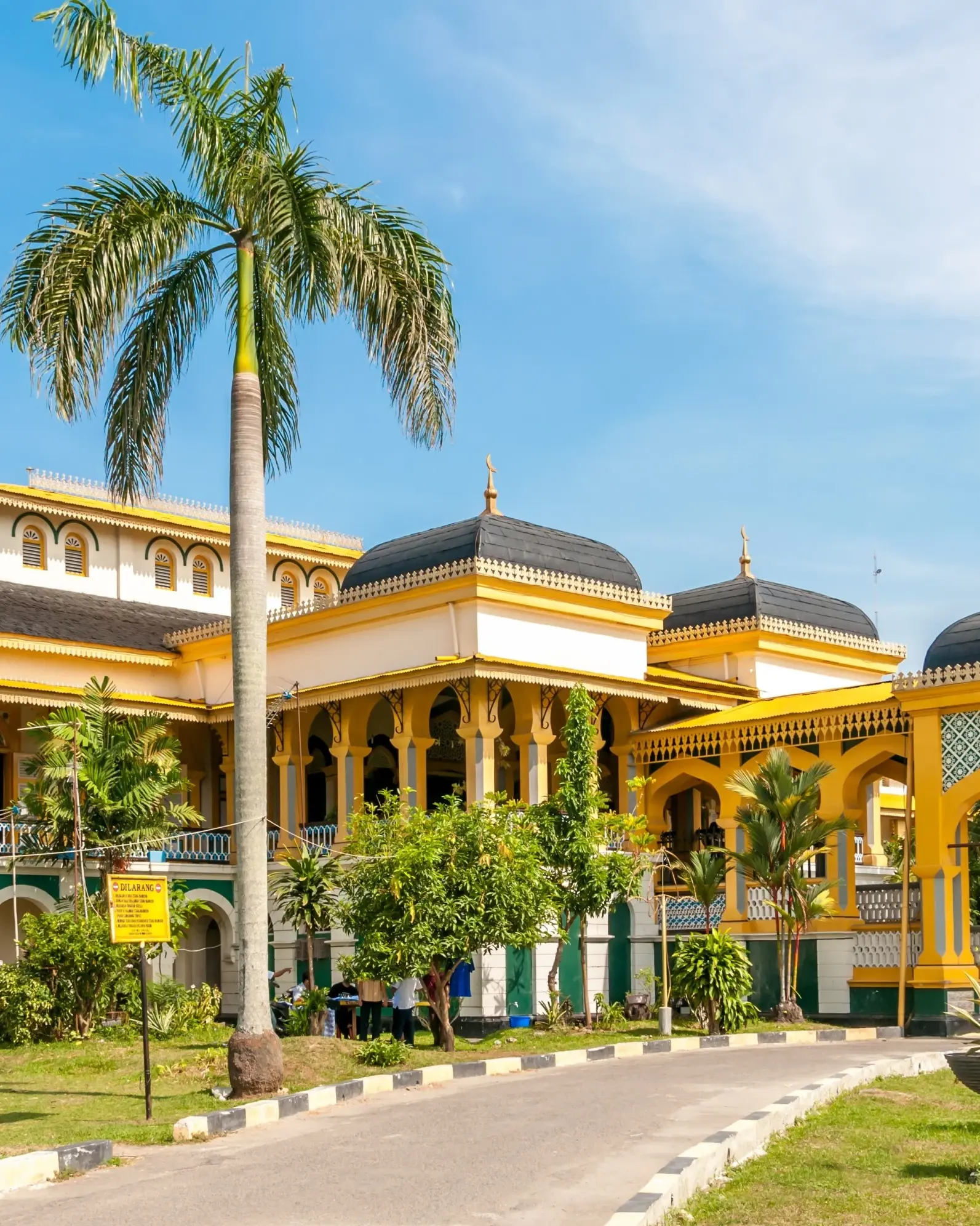 The ornate, bright-yellow Maimun Palace with palm trees out front, Medan, Indonesia. Image credit: stock.adobe.com