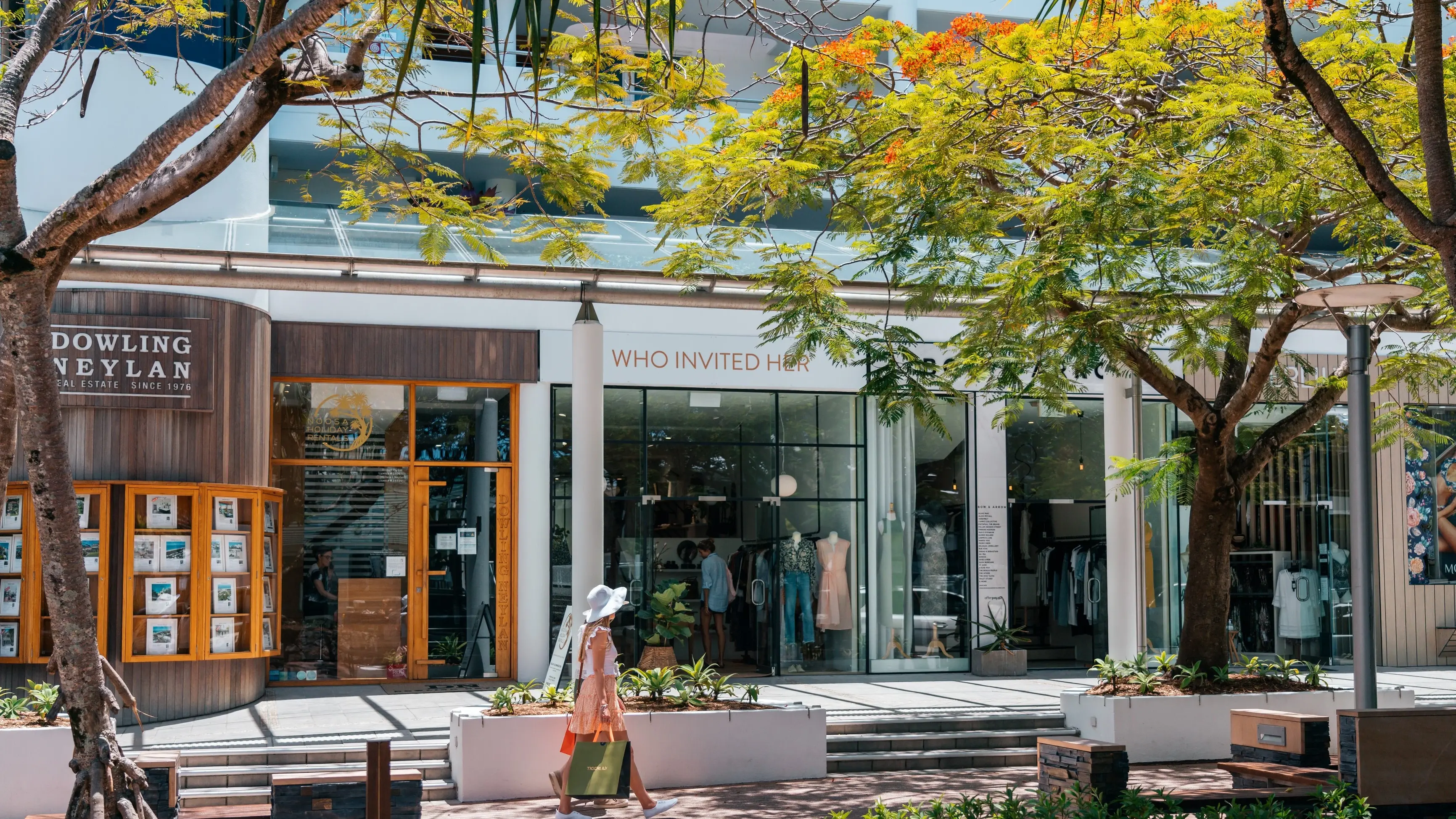 Two people with shopping bags walk past boutiques on tree-lined Hastings Street in Noosa. Image credit: Tourism and Events Queensland