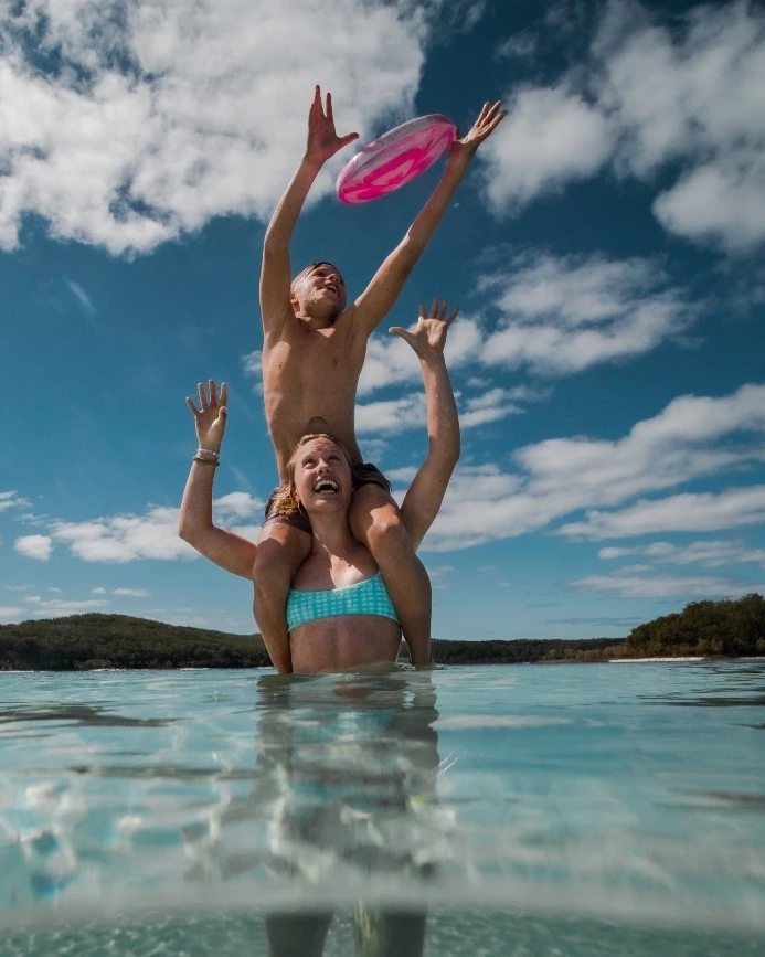 Woman in the water with child on shoulders playing with inflatable ring at Lake McKenzie, K'gari (Fraser Island). Image credit: Tourism and Events Queensland