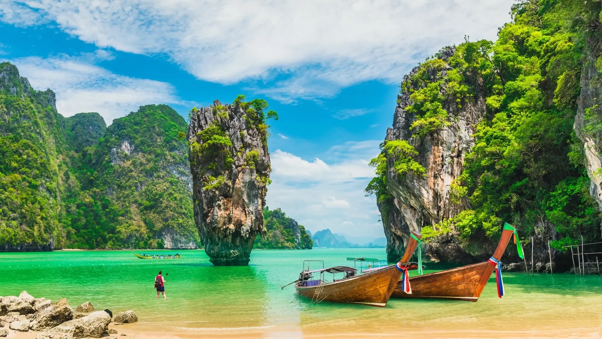 Two longtail boats moored at the beach and a person standing in the water at Phang Na Bay, Thailand. Image credit: Shutterstock