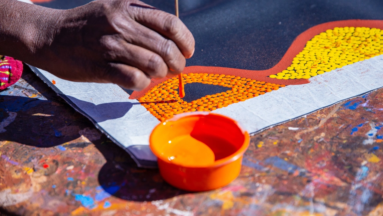 Close up of artist creating dot painting at Maruka Arts, Uluru, Northern Territory. Image credit: Tourism NT/Felix Baker