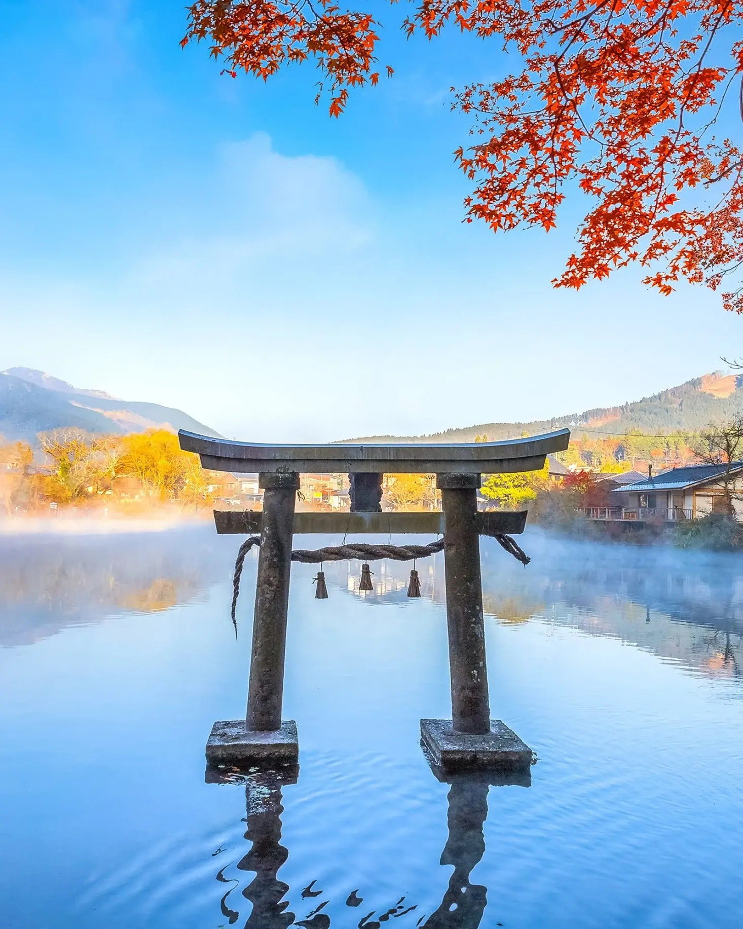 Torii temple gate in the reflective Lake Kinrinko in Yufuin, Oita with a blue sky and trees with autumn leaves. Image credit: stock.adobe.com