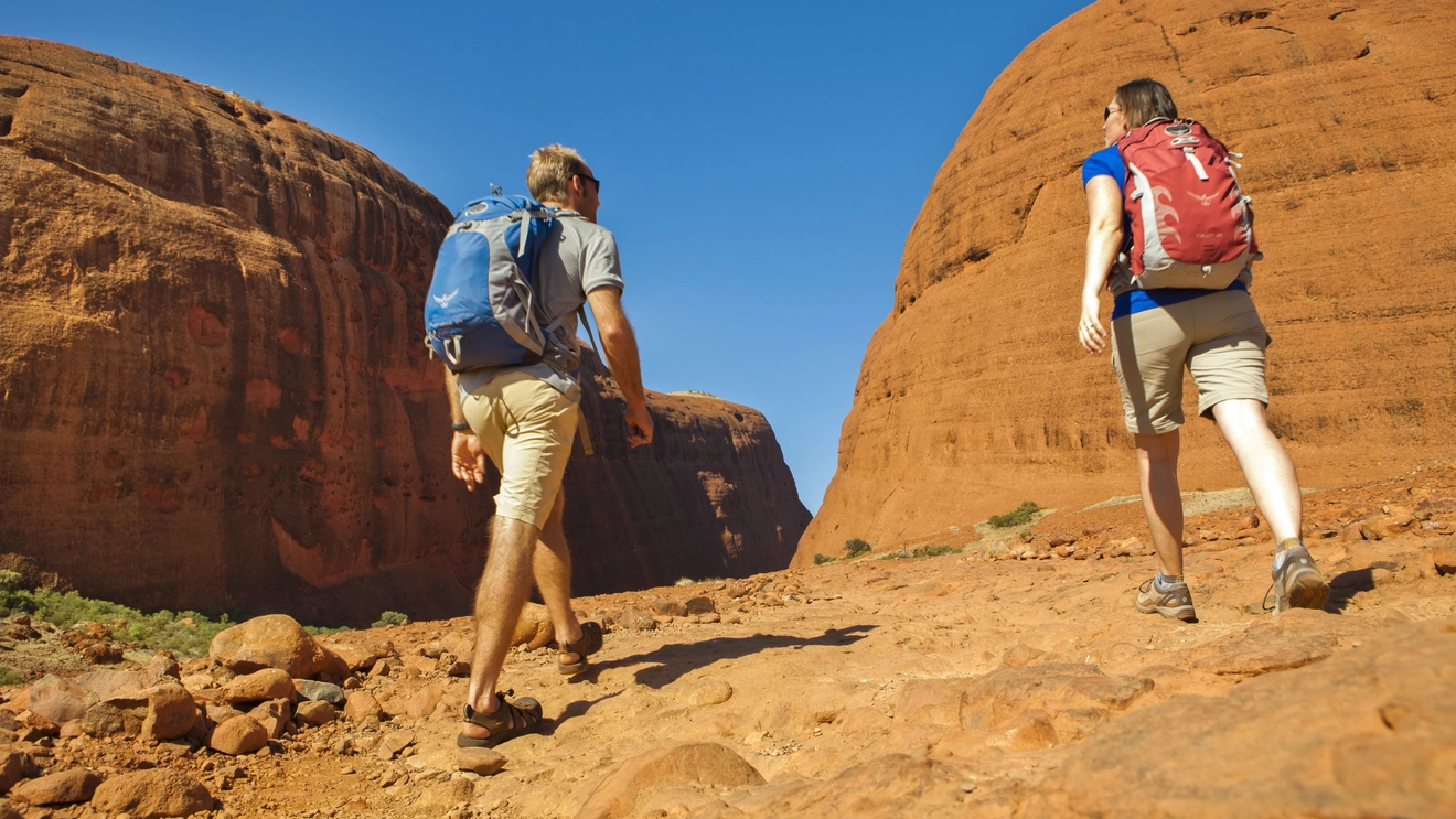 Two people hiking at Kata Tjuta on a sunny, blue-sky day. Image credit: Tourism NT/Paddy Pallin