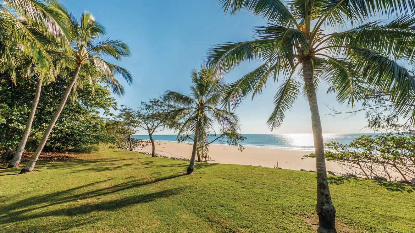 Lawn and palm trees line the white sand and calm water at Blacks Beach, Mackay. Image credit: Tourism and Events Queensland