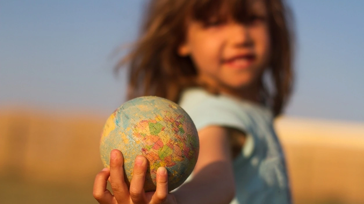 Close up of a coloured world globe being held by a child who is blurred in the background. Image credit: iStock