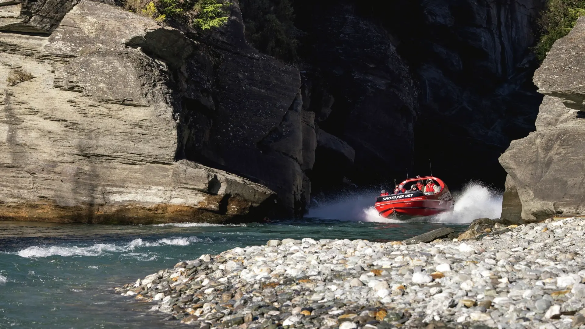 The red Shotover Jet boat emerges from a canyon into some gentle rapids, Queenstown, New Zealand. Image credit: Miles Holden/Tourism NZ