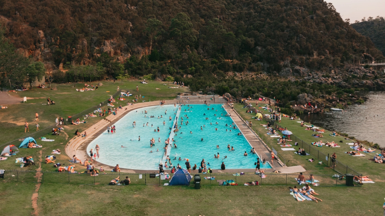 People in a bright blue swimming pool surrounded by grass, by a lake in Cataract Gorge, near Launceston, Tasmania. Image credit: Tourism Tasmania/Jarrad Seng