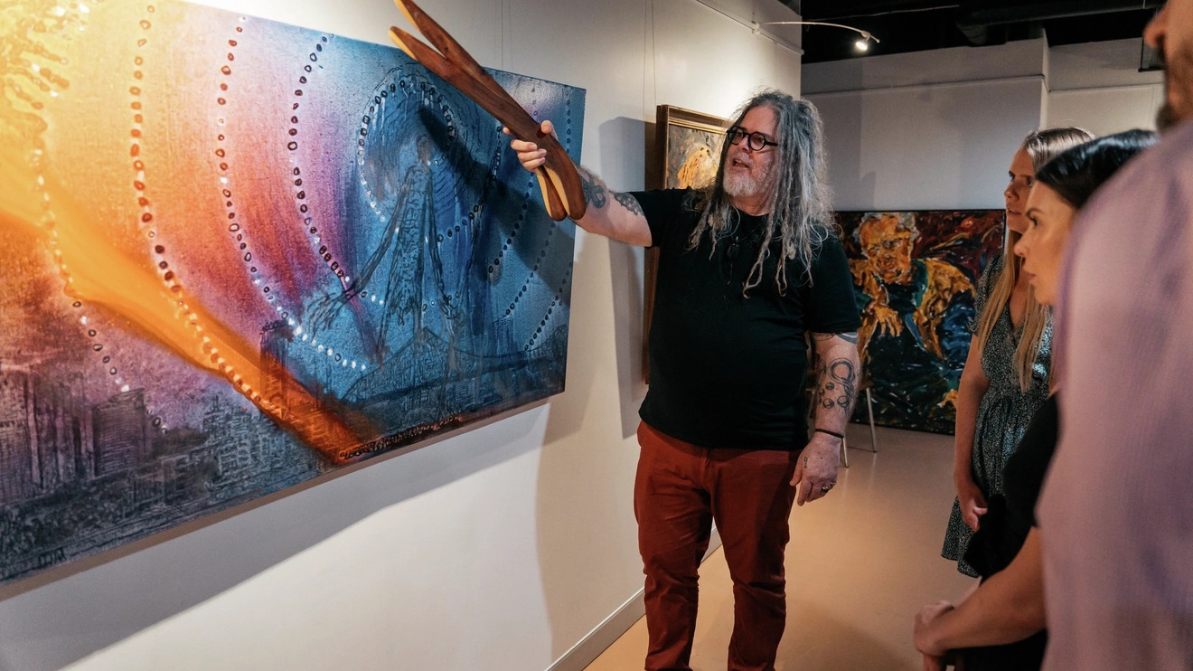 First Nations artist explaining his painting to tourists at Birrunga Aboriginal art gallery, Brisbane. Image credit: Tourism and Events Queensland.