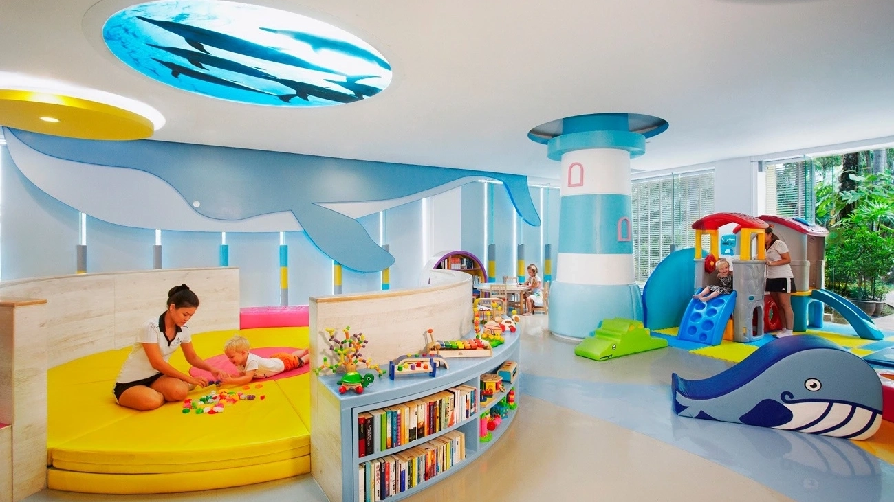 A babysitter plays with a small child in a colourful kids club