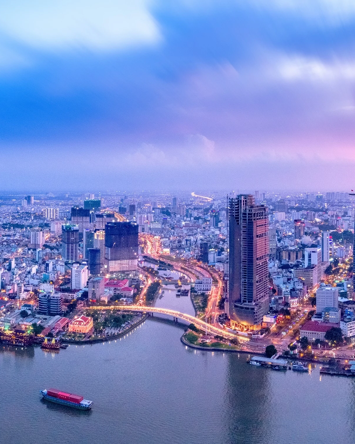 Aerial view of skyscrapers and city lights in Ho Chi Minh City’s financial and business districts, with Saigon River in the foreground, at dusk. Image credit: stock.adobe.com