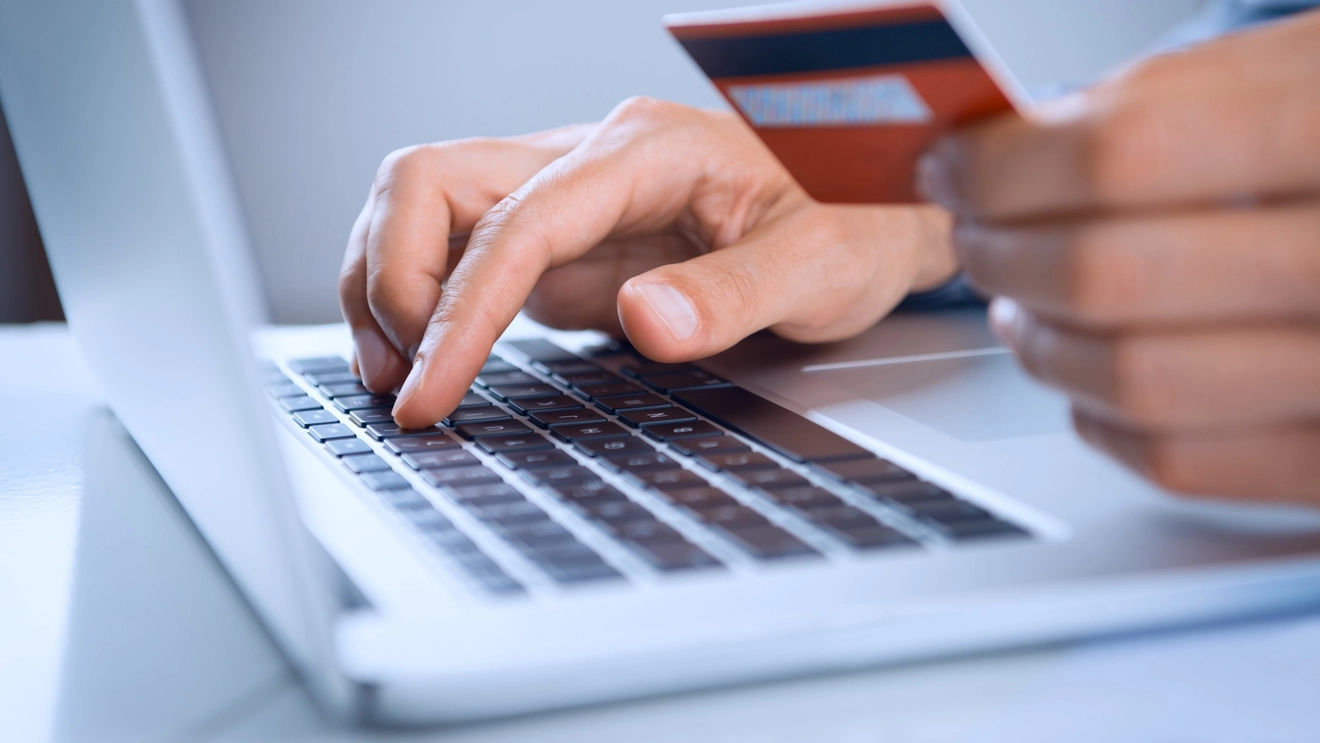 Someone holds a credit card while typing on a laptop