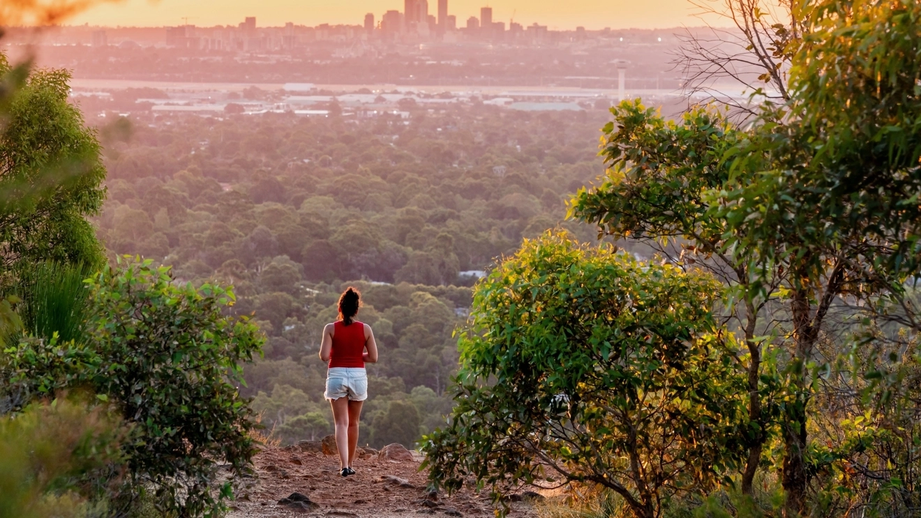 Young woman gazes at distant view of Perth city skyline from the Kalamunda National Park. Image credit: bmphotographer