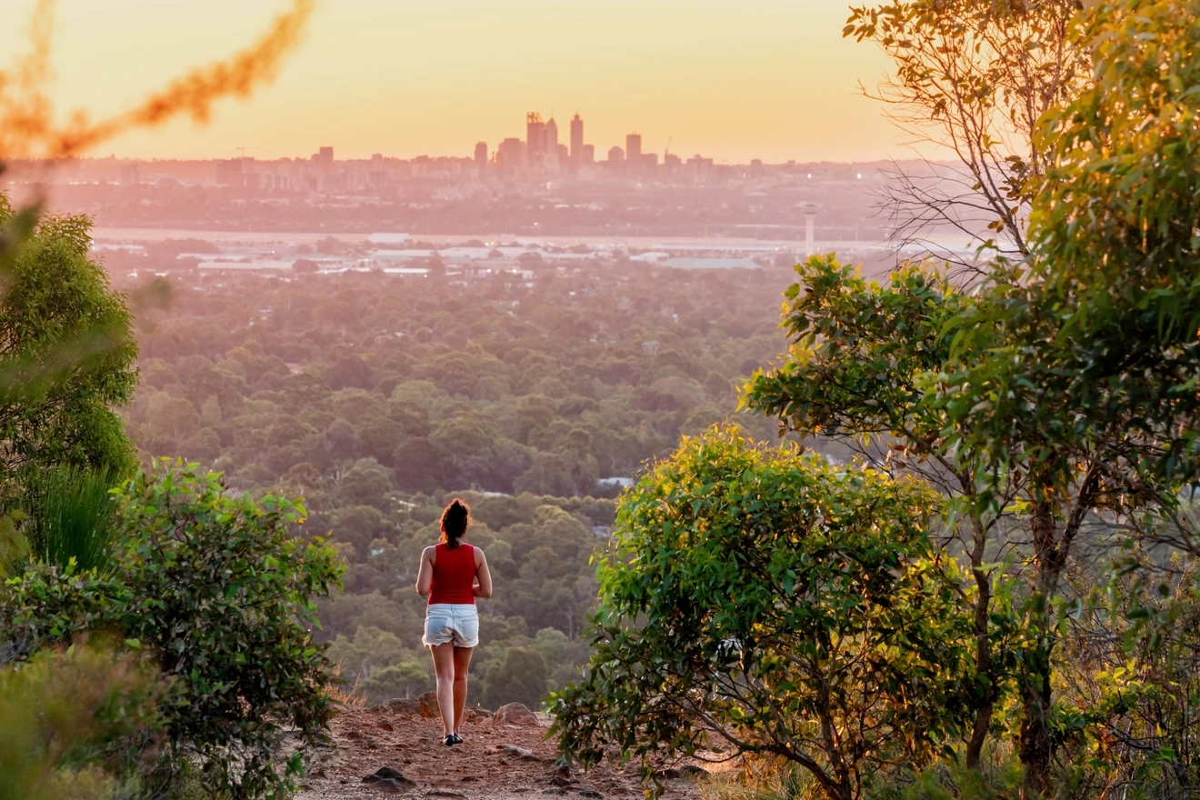 Young woman gazes at distant view of Perth city skyline from the Kalamunda National Park. Image credit: bmphotographer