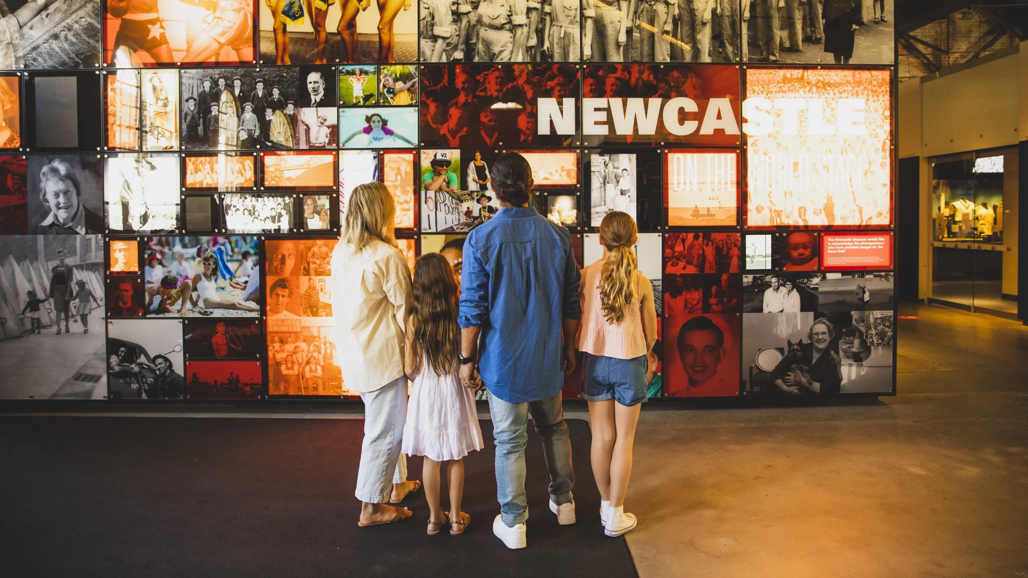 The back view of a family looking at a wall of historical Newcastle images at the Museum. Image credit: Destination NSW