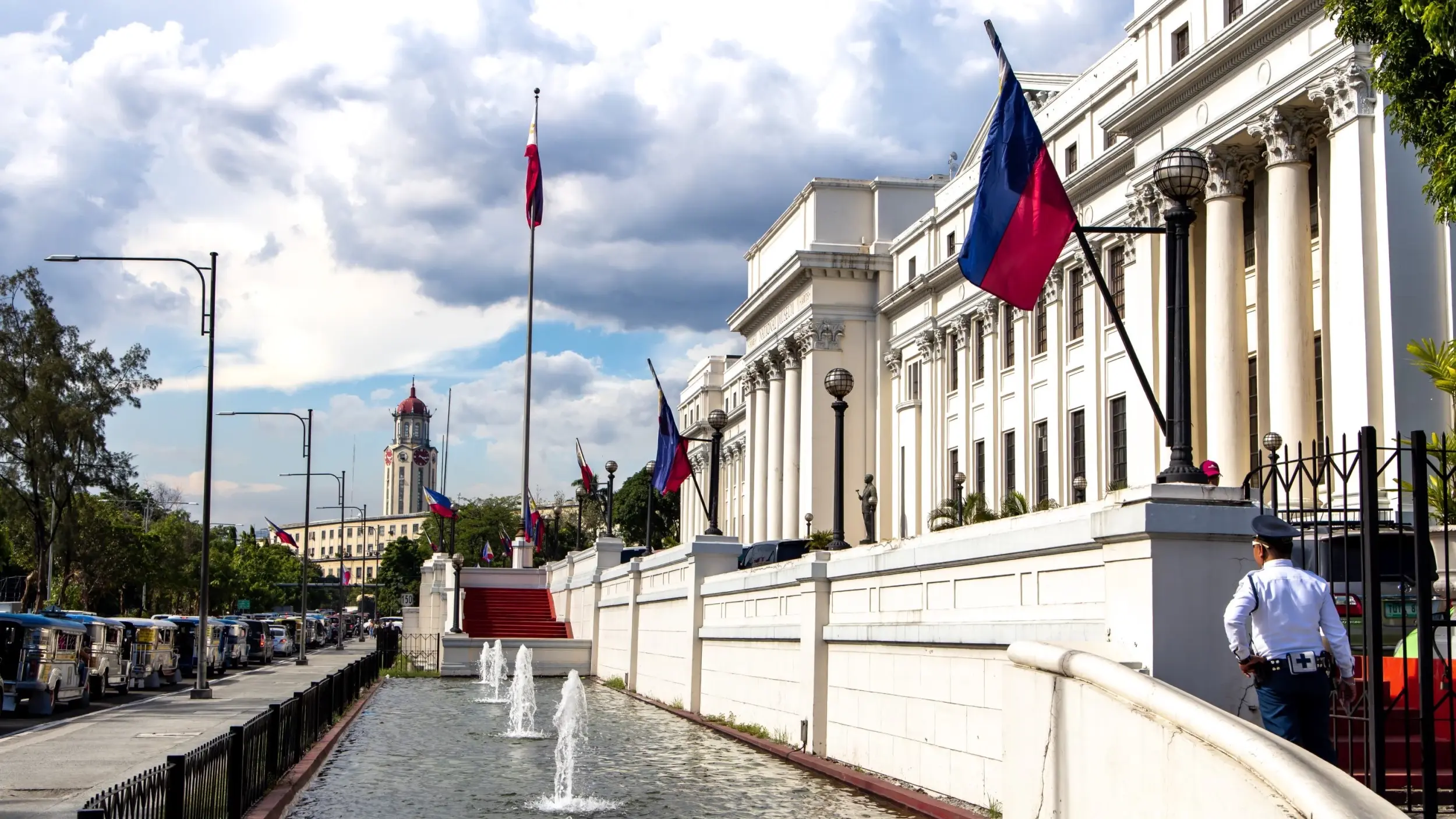 Exterior view of tall, white National Museum of Fine Arts building adorned with Filipino flags, and with fountains in shallow pool in front. Image credit: stock.adobe.com