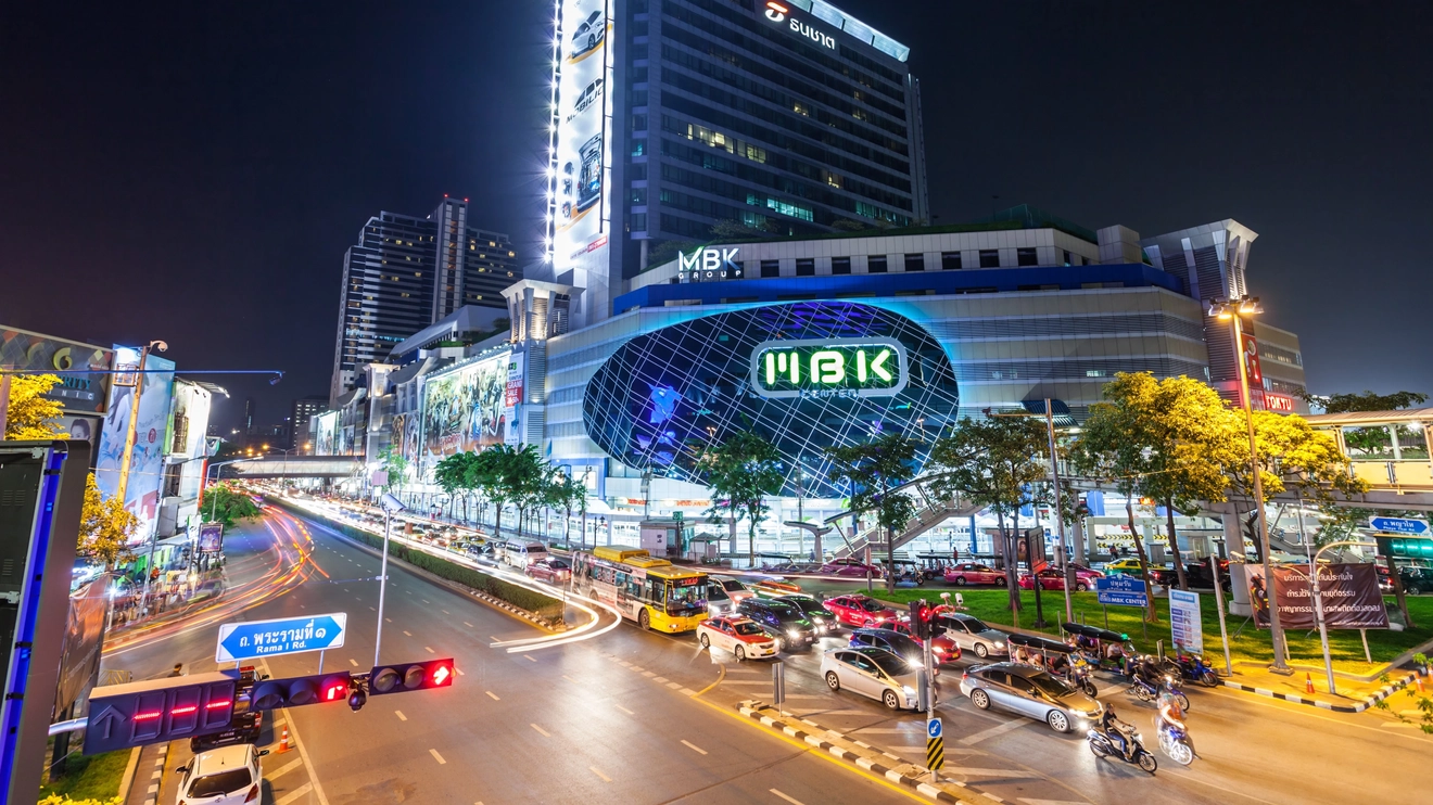 The modern exterior of MBK Center, illuminated at night with traffic in front, Bangkok, Thailand. Image credit: saiko3p – stock.adobe.com