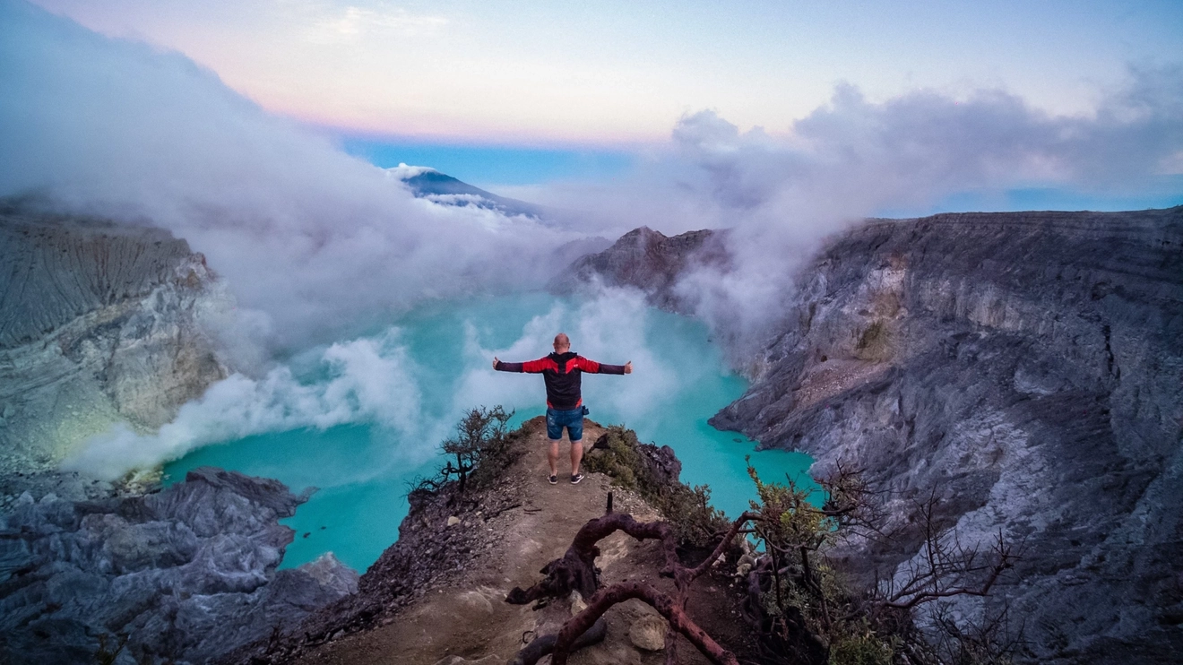 Person standing on the edge of Mount Ijen volcanic crater with blue-coloured lake and sulfur gas below. Image credit: stock.adobe.com