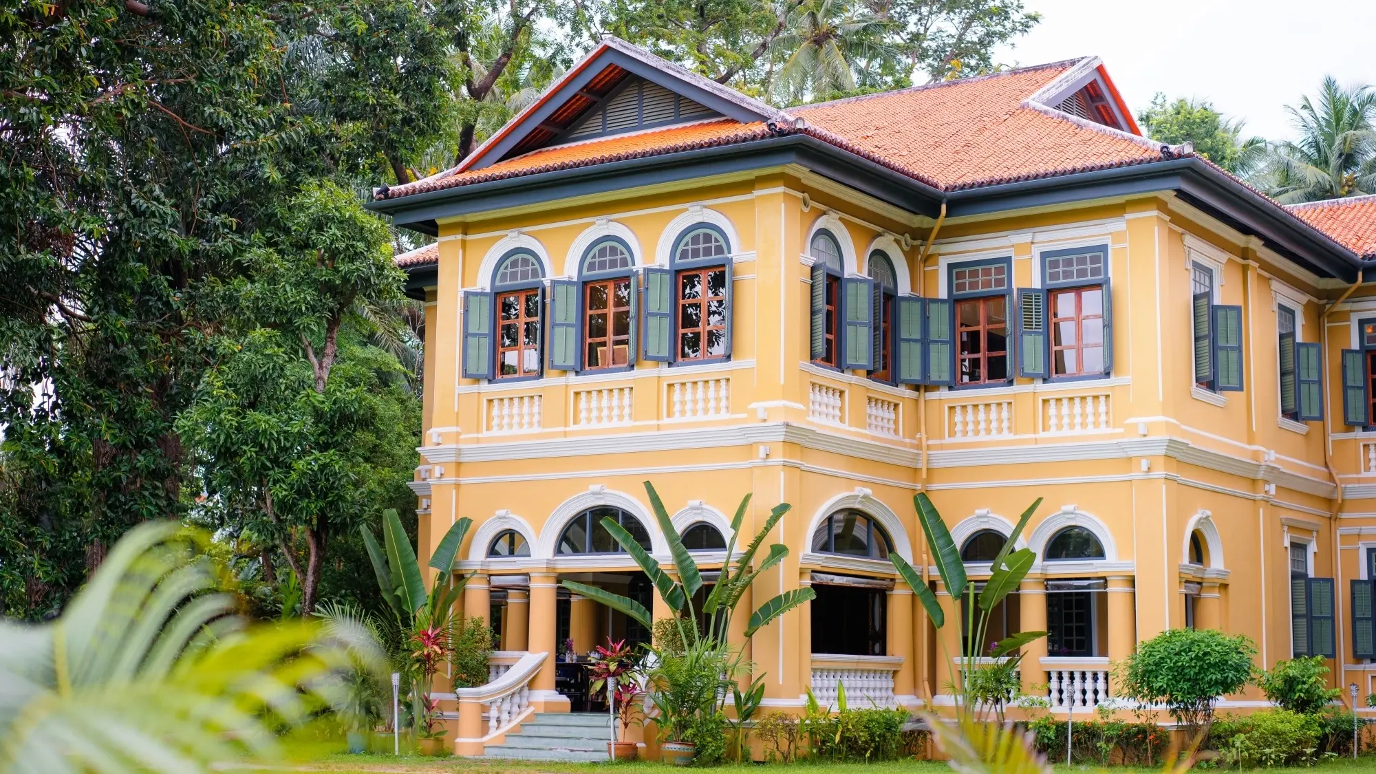 Façade of a colonial-style building painted orange with white details surrounded by lush garden. Image credit: Shutterstock