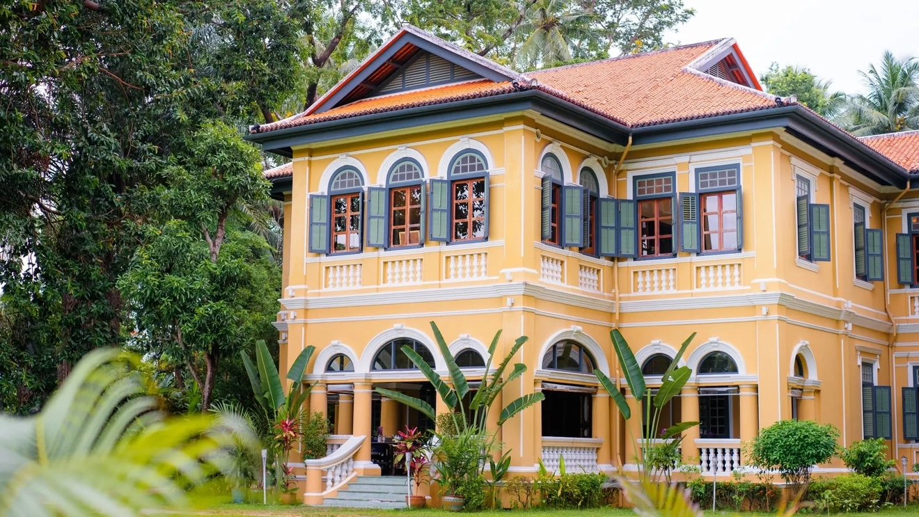 Façade of a colonial-style building painted orange with white details surrounded by lush garden. Image credit: Shutterstock