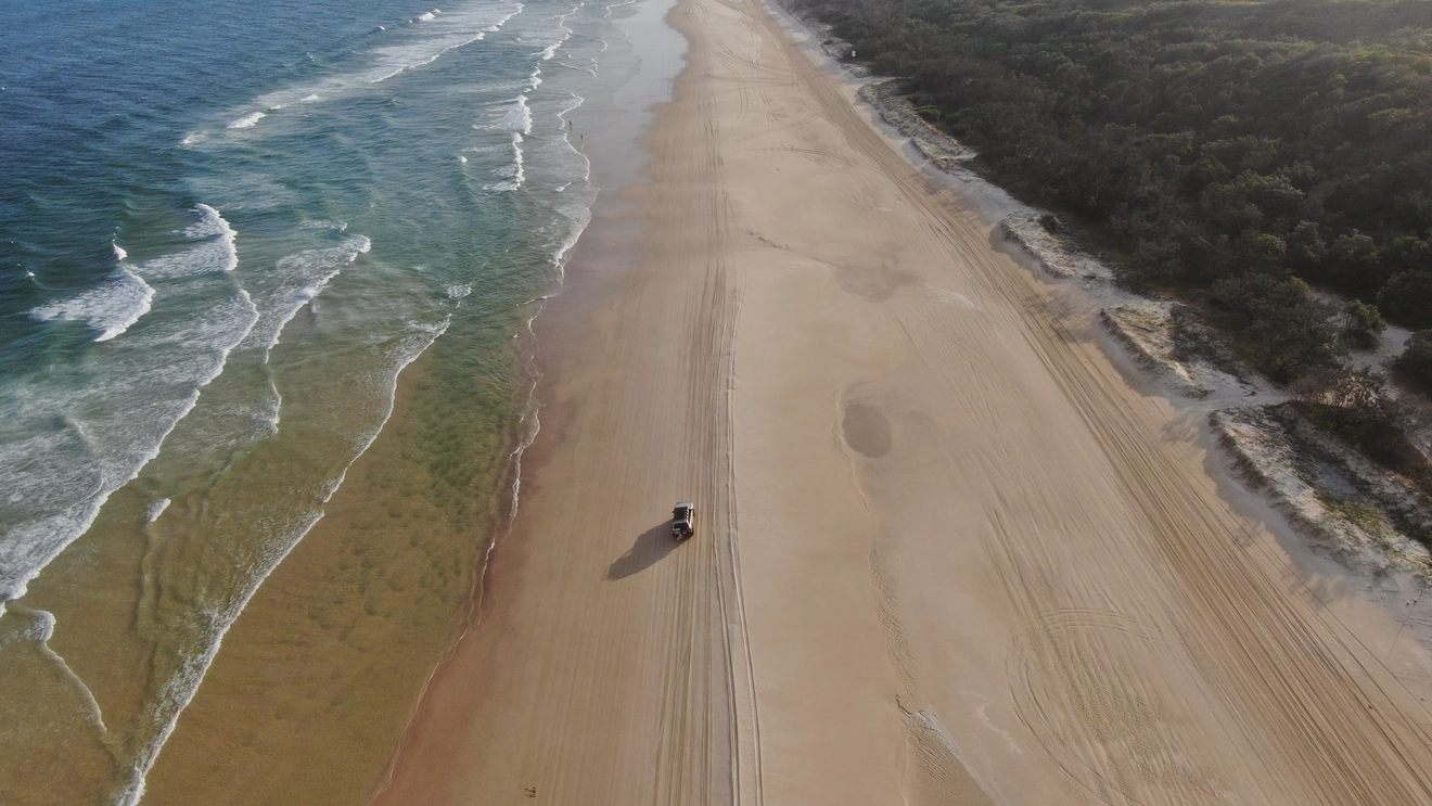 Aerial view of 4WD driving along 75 Mile Beach, K'gari (Fraser Island). Image credit: Tourism and Events Queensland