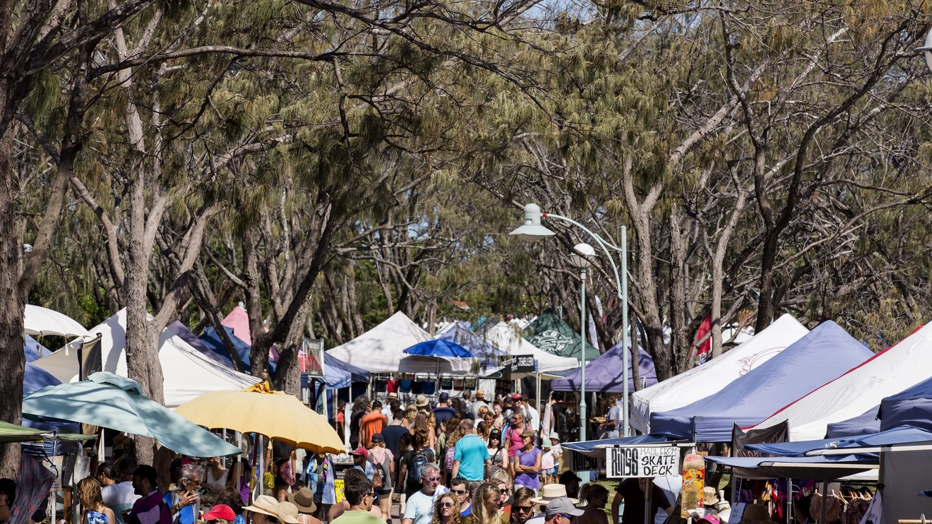 People browsing stalls framed with trees at Byron Community Market. Image credit: Destination NSW
