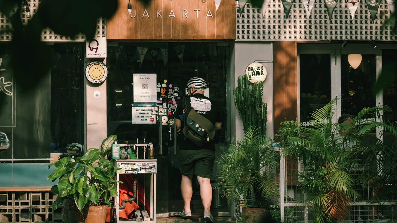 Exterior of Brookland Coffee, with large pot plants in the foreground and cyclist entering front door, Jakarta. Image credit: Brookland Coffee