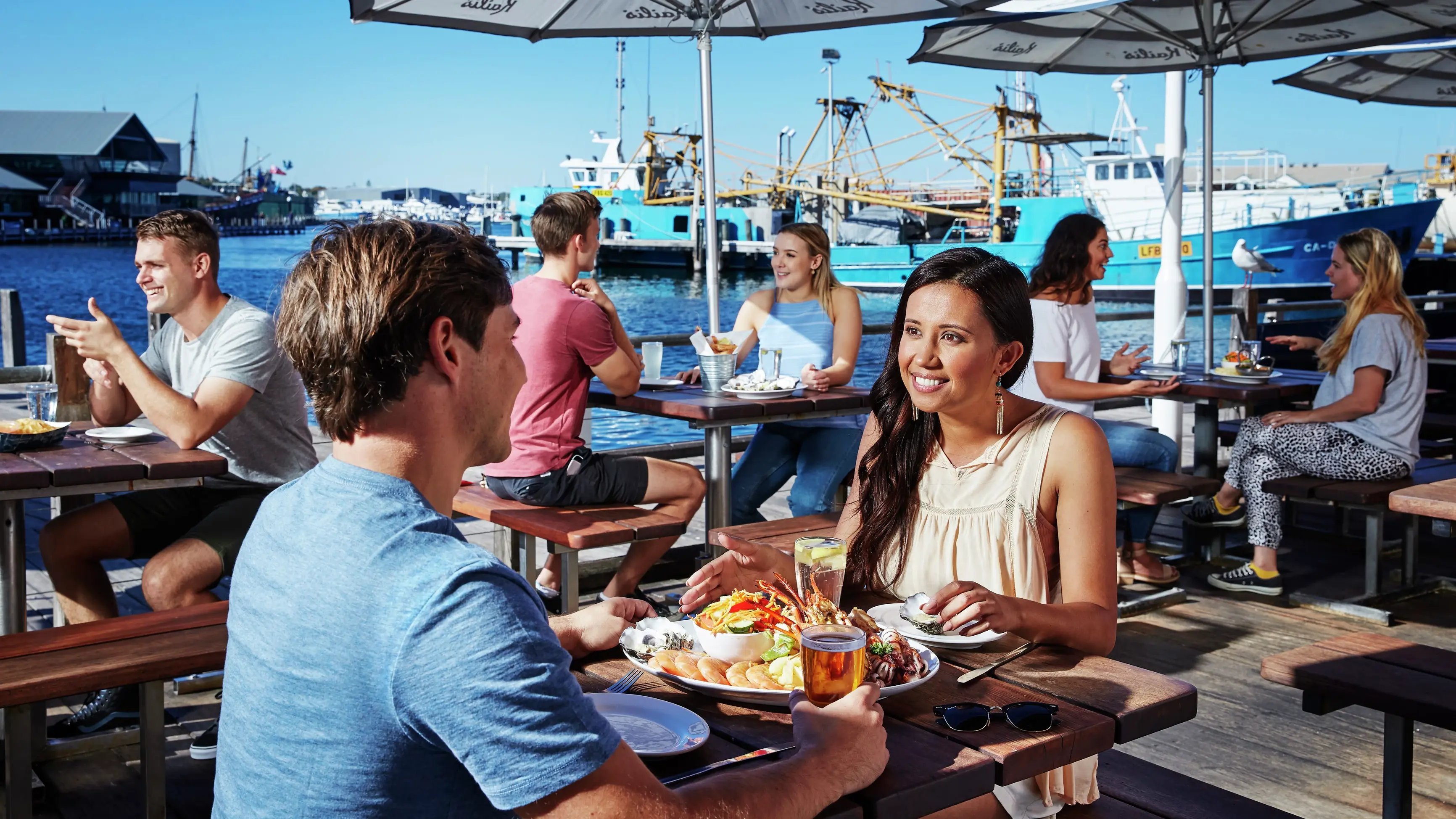 Couple enjoying fresh local seafood on outside deck at Fremantle Fishing Boat Harbour. Image credit: Tourism Western Australia