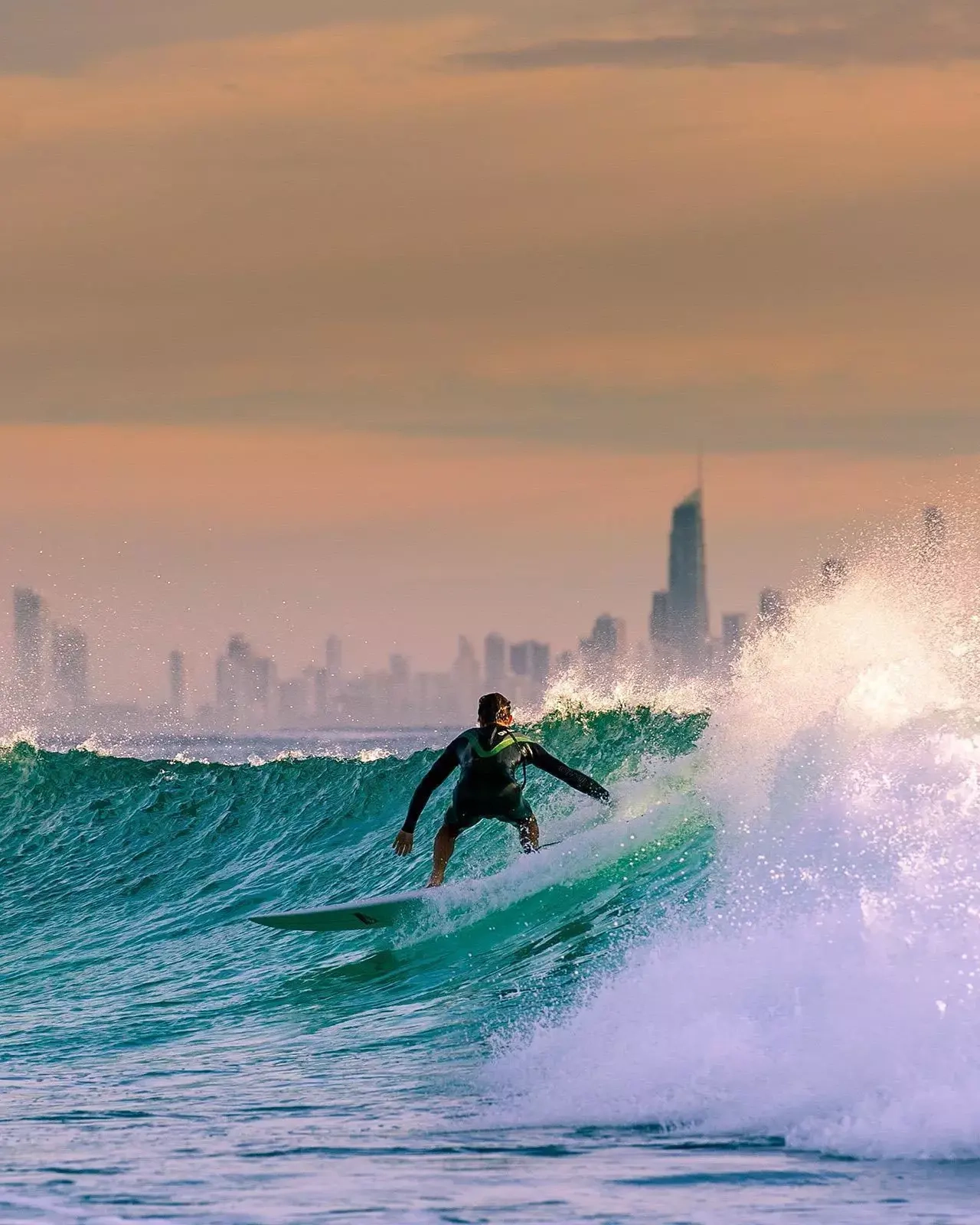 A surfer rides a wave with a skyline of Surfers Paradise hotels behind it. Image credit: Shutterstock