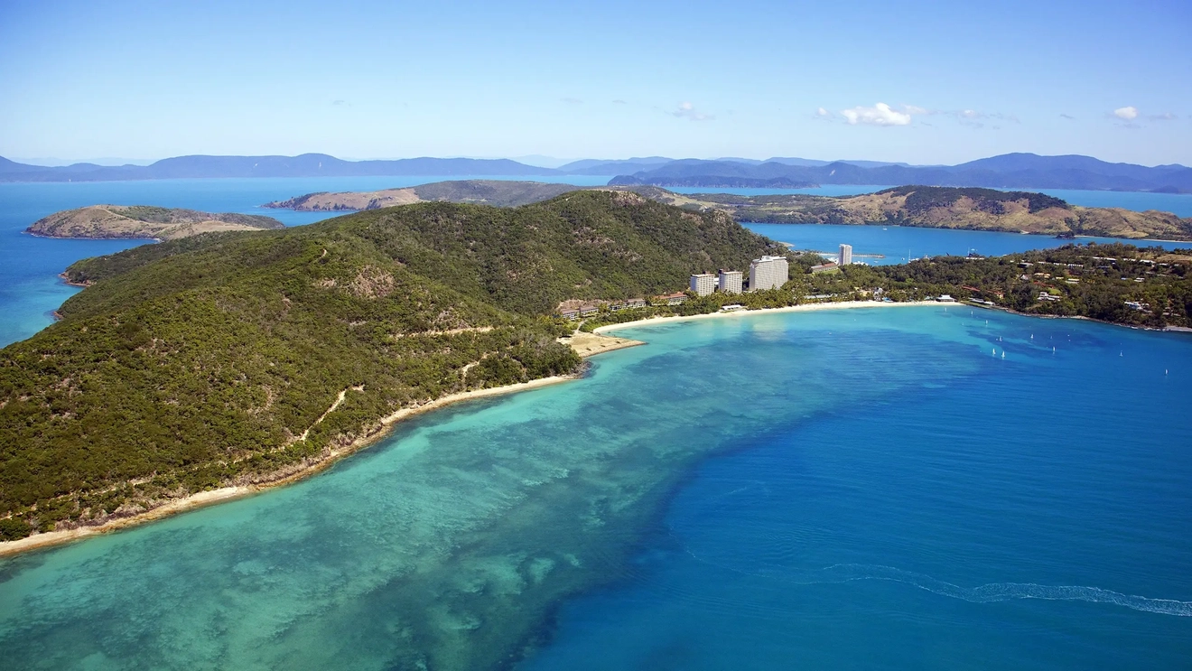 Aerial shot of foliage-covered Hamilton Island fringed with beaches and resorts, surrounded by bright blue water. Image credit: Shutterstock