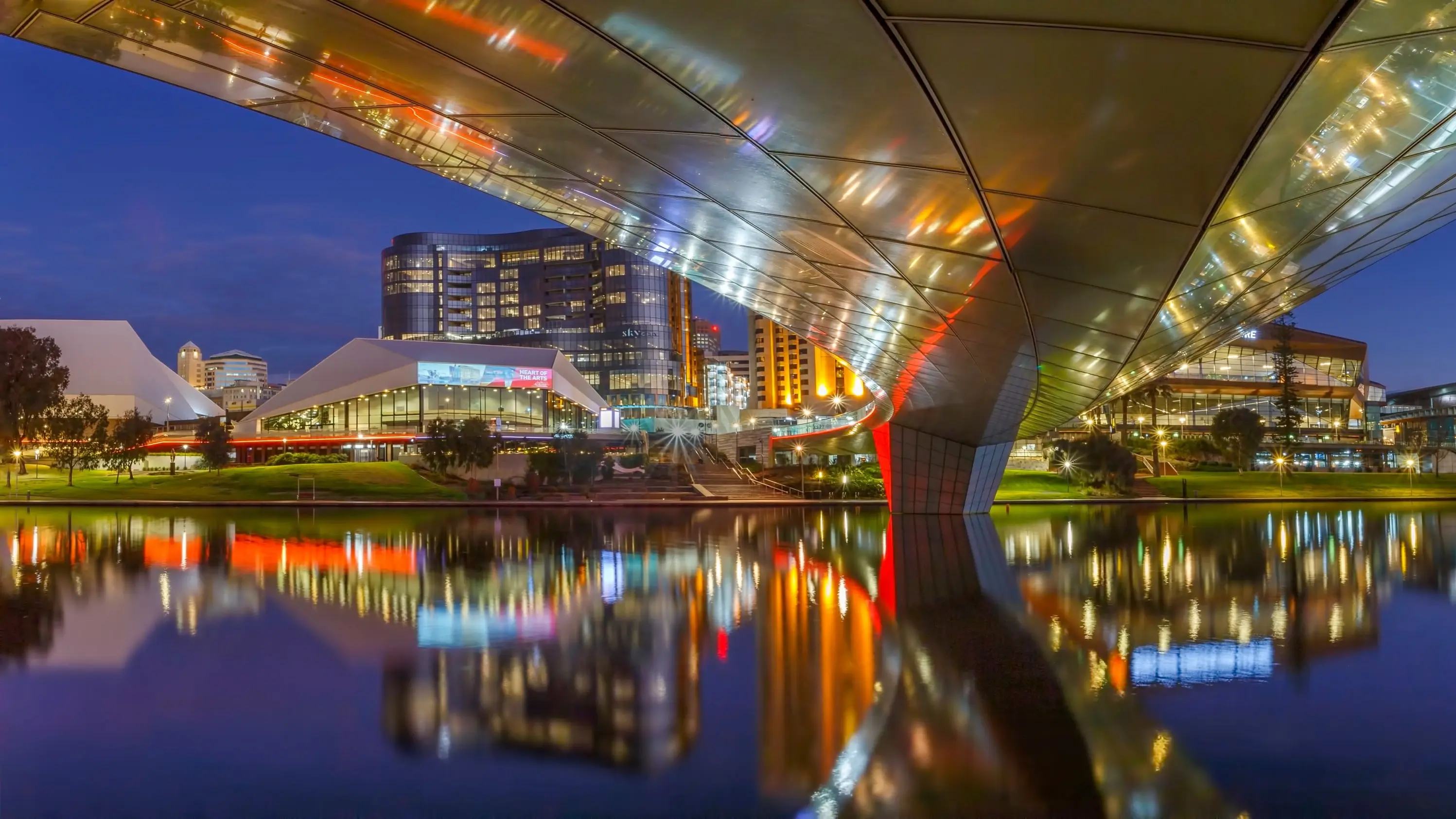 View from under the Riverbank Bridge of the Riverbank Precinct skyline at night and its reflection on the River Torrens, Adelaide. Image credit: South Australia Tourism Commission
