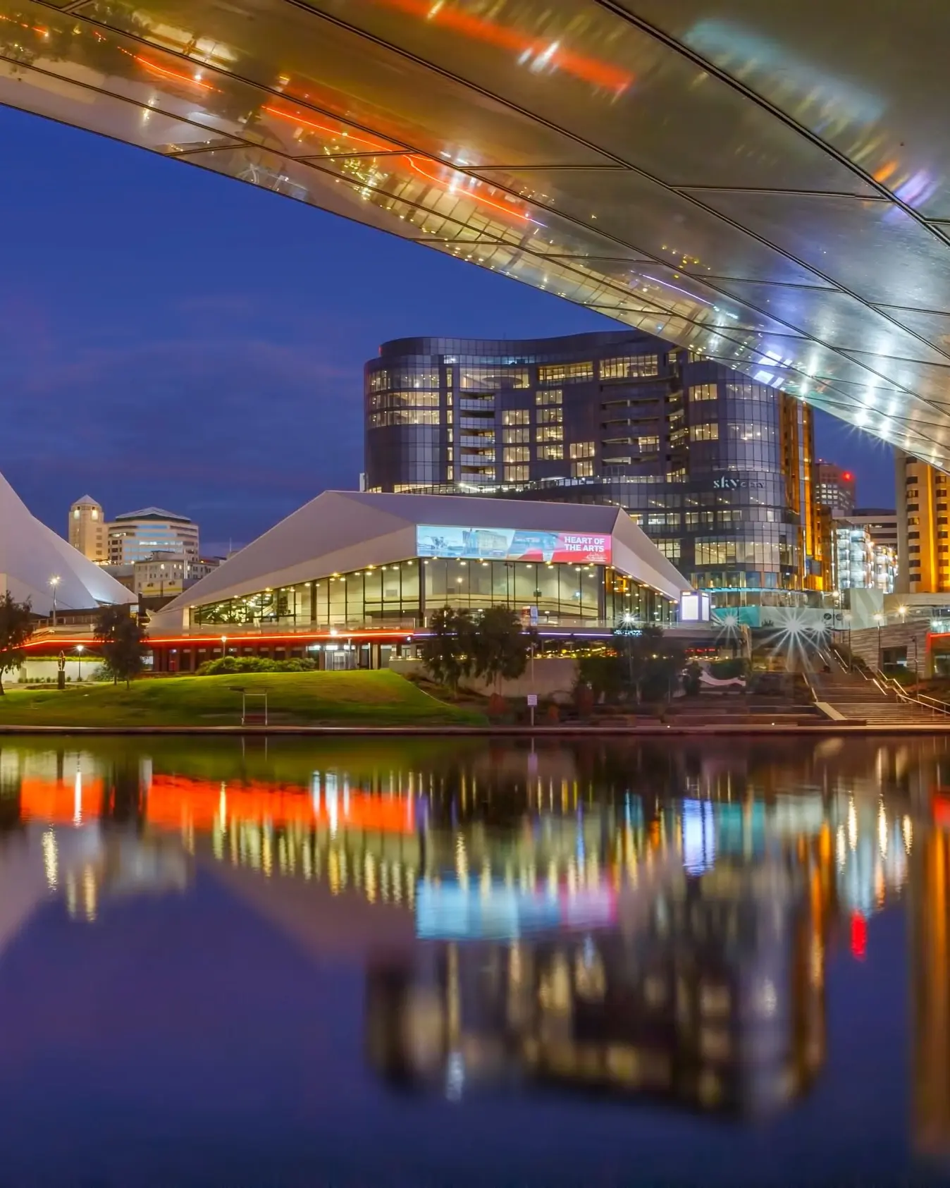 View from under the Riverbank Bridge of the Riverbank Precinct skyline at night and its reflection on the River Torrens, Adelaide. Image credit: South Australia Tourism Commission