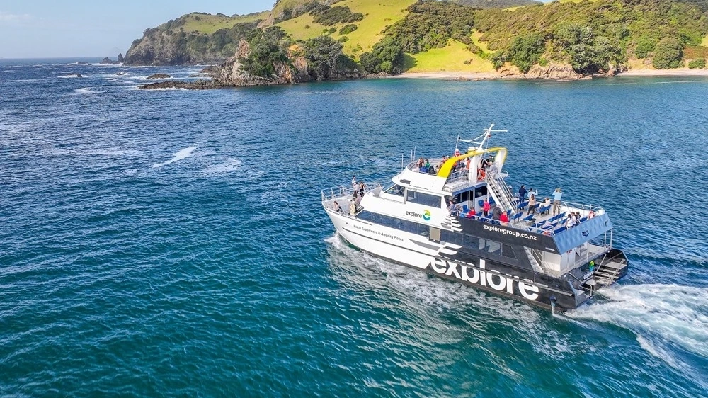 People on a double-decker sightseeing boat on the water with green hills in the background.