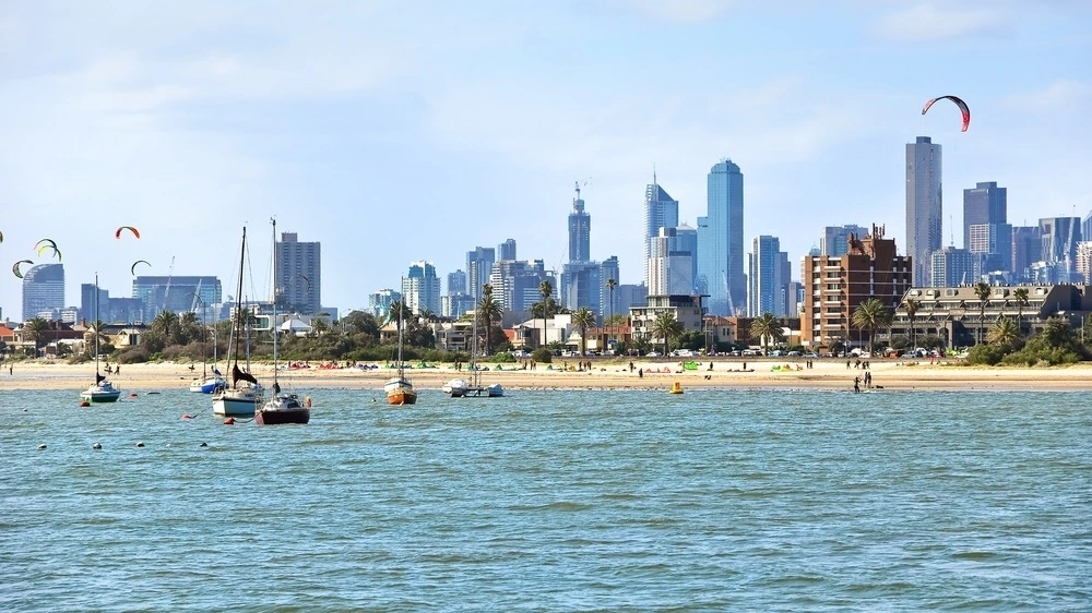 St Kilda Beach, with boats on the water, kites in the sky, and the Melbourne city skyline in the background.