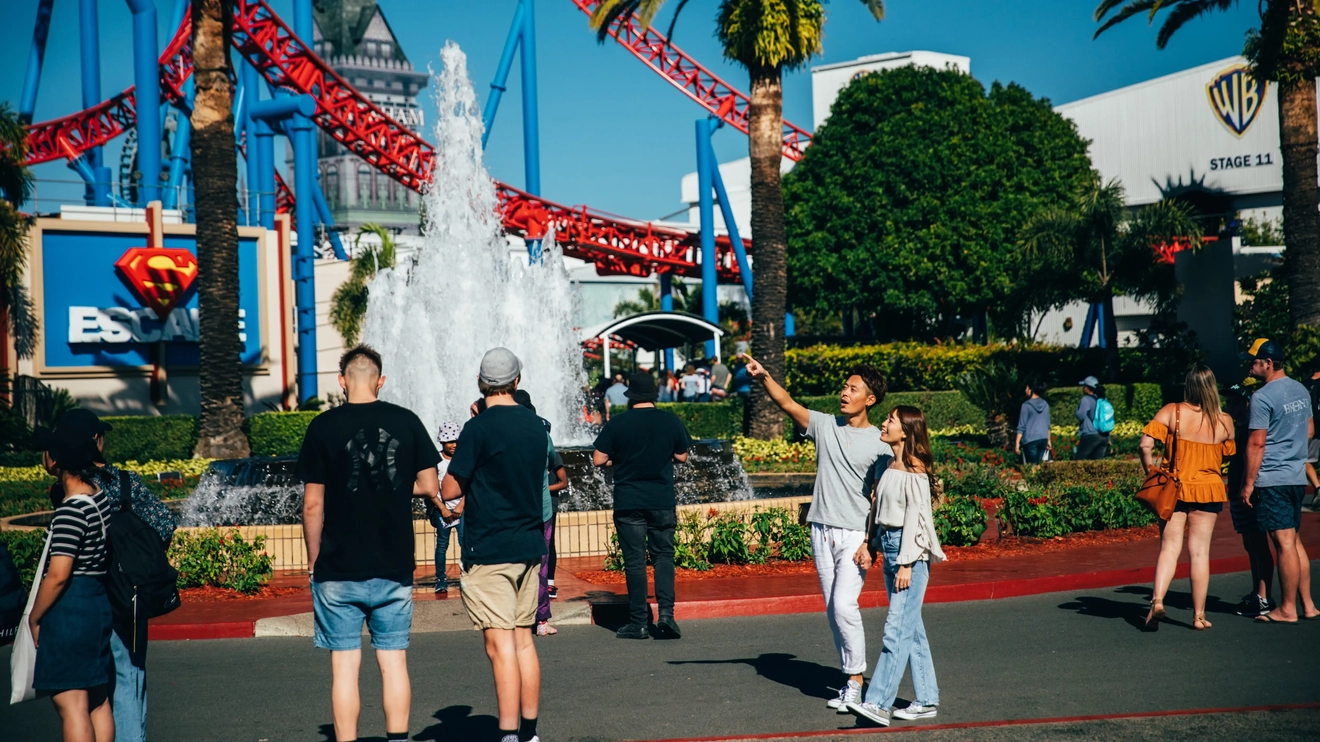 People walking around Warner Bros. Movie World with rollercoaster and movie studio in background. Image credit: Destination Gold Coast