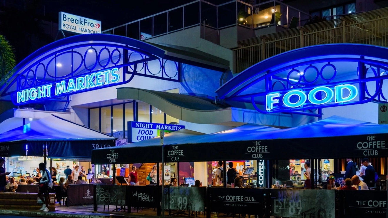 People sitting outside the blue neon exterior of Cairns Night Markets, Tropical North Queensland.