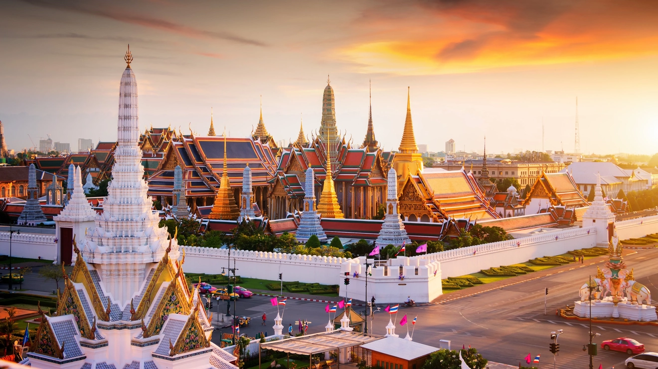 Exterior of the Royal Palace complex, with ornate white walls and golden spires, surrounded by a white fence, in Bangkok, Thailand. Image credit: stock.adobe.com