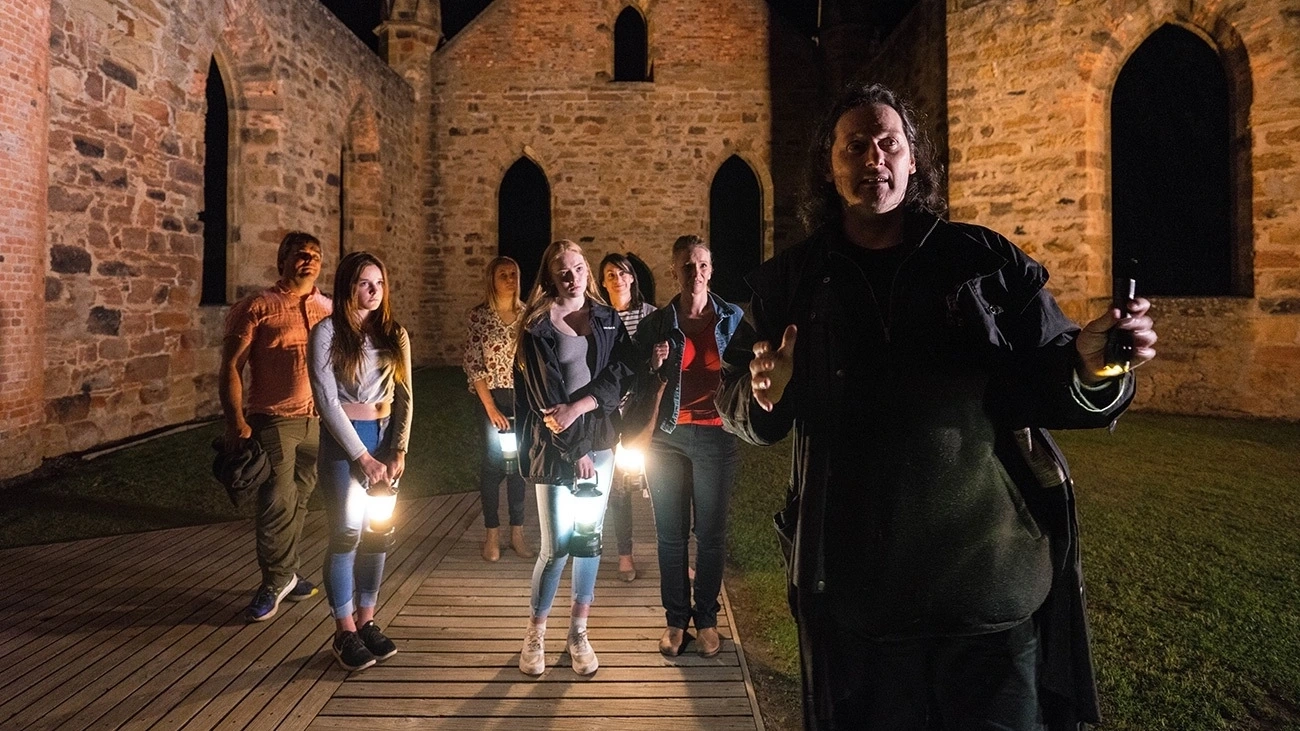 A man in costume guides a group of young people at a ghost tour in Port Arthur, Tasmania.
