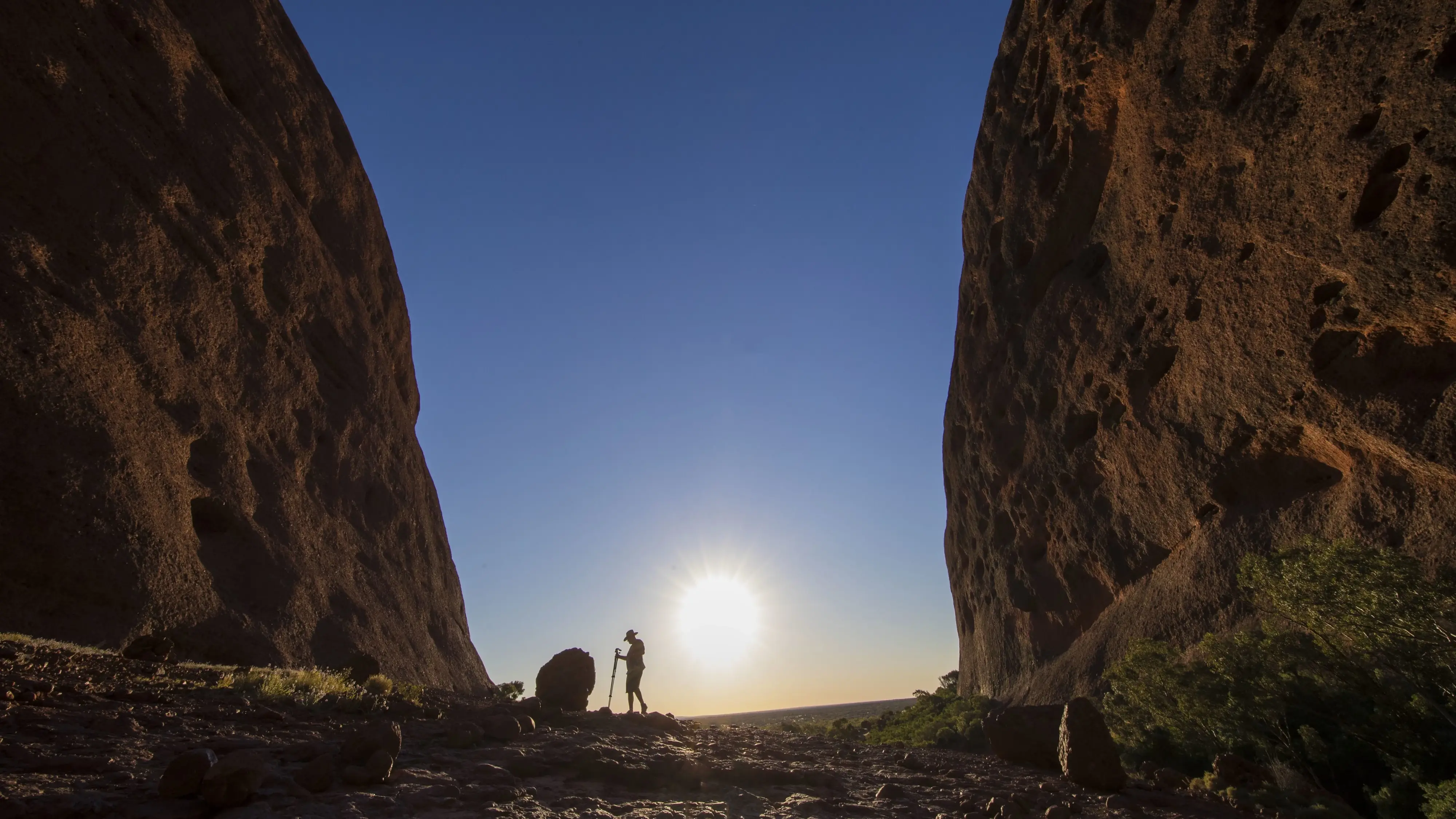 Silhouette of a hiker at sunrise in between two enormous rock formations at Kata Tjuta. Image credit: Tourism NT/Sean Scott
