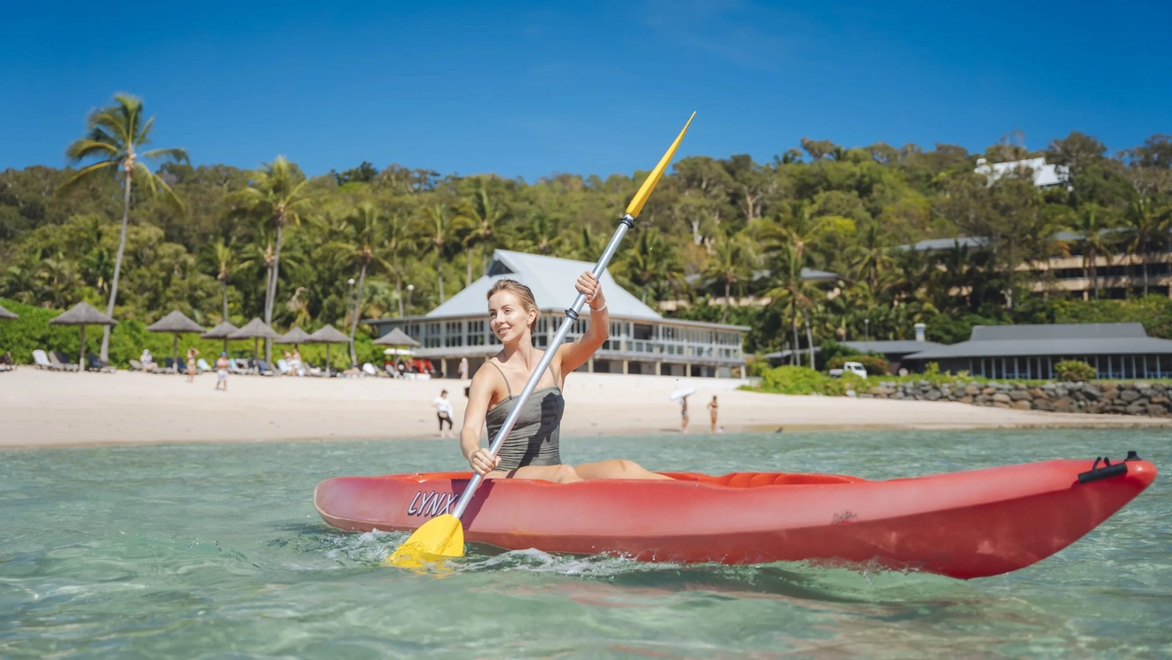 A person smiling and kayaking on blue water on a sunny day. Image credit: Tourism and Events Queensland