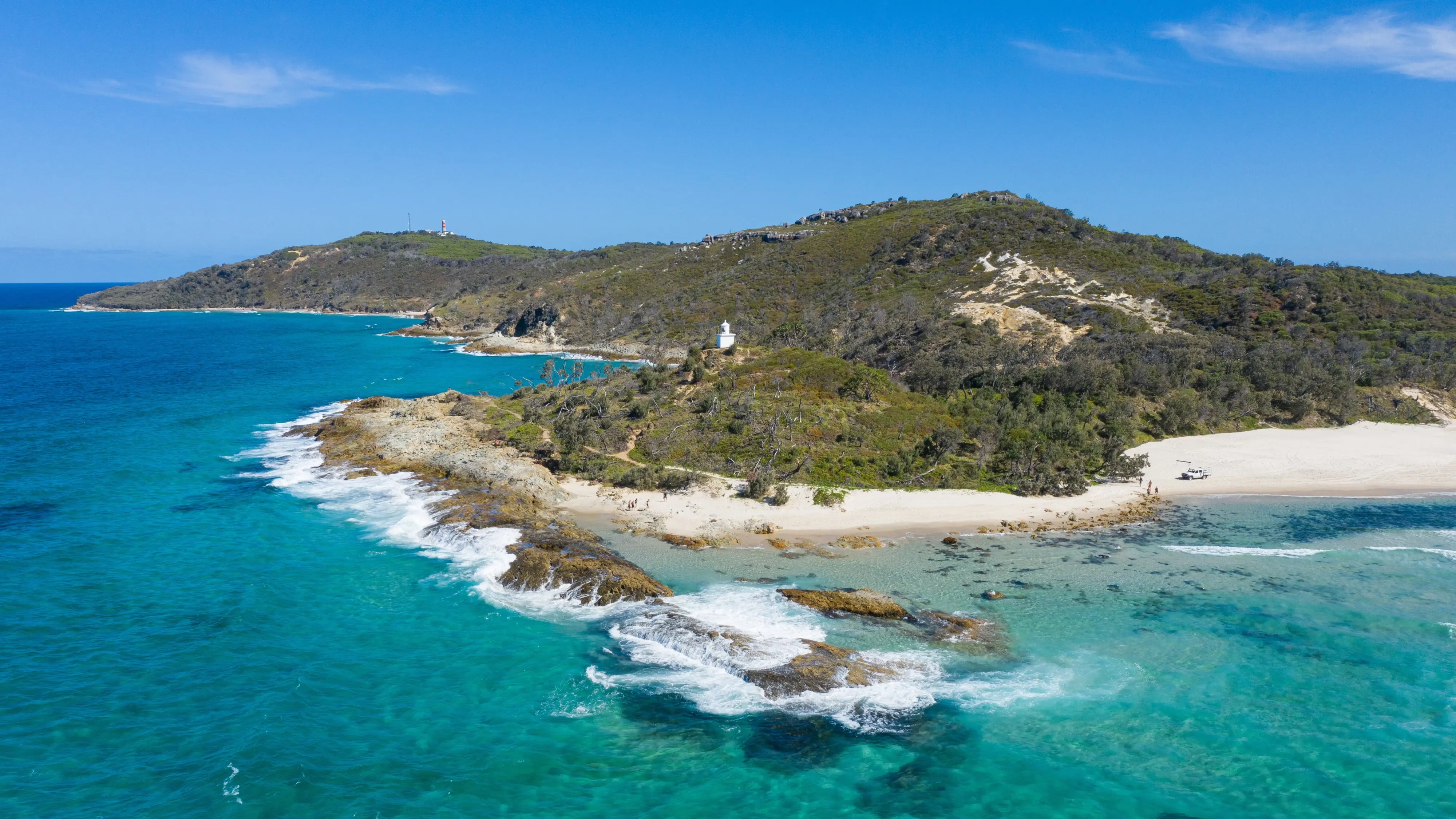 Tree-covered Moreton Island in the sun, with sandy shore and turquoise waters. Image credit: Tourism and Events Queensland