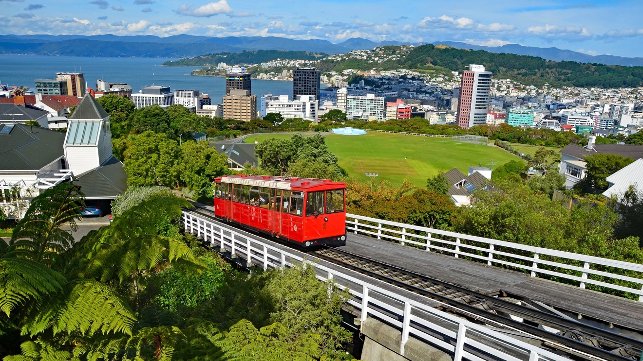The red Wellington Cable Car on its hillside track with views of the city and harbour in the background, Wellington, New Zealand. Image credit: stock.adobe.com