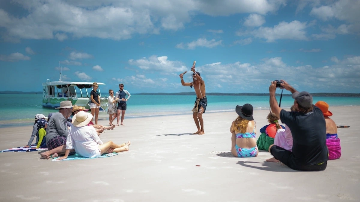 Tour group watching a Butchulla man perform a traditional dance on the beach with Turtle Discovery Eco Tour, Great Sandy Marine Park.