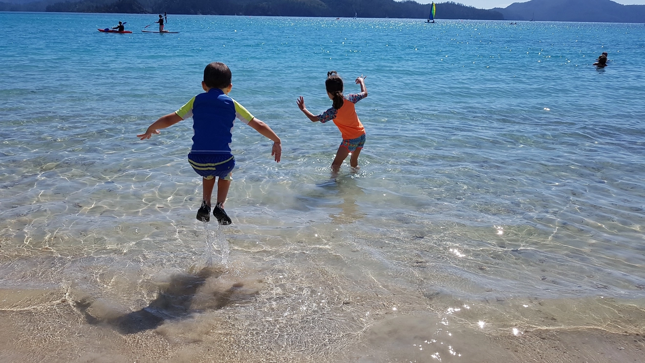 Two small children jumping in the water at Catseye Beach, Hamilton Island. Image credit: Shutterstock