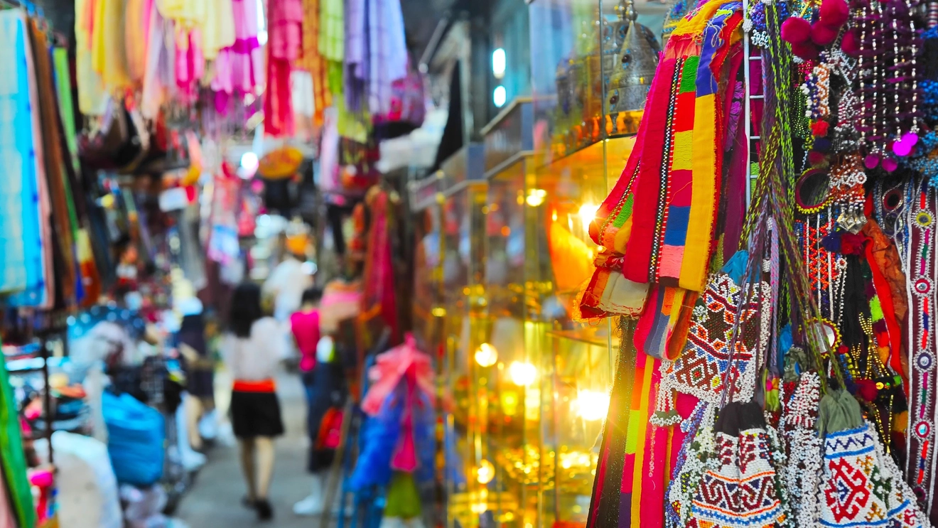 Colourful beaded bags and hanging clothes in a row of market stalls at Chatuchak Market, Bangkok, Thailand. Image credit: stock.adobe.com