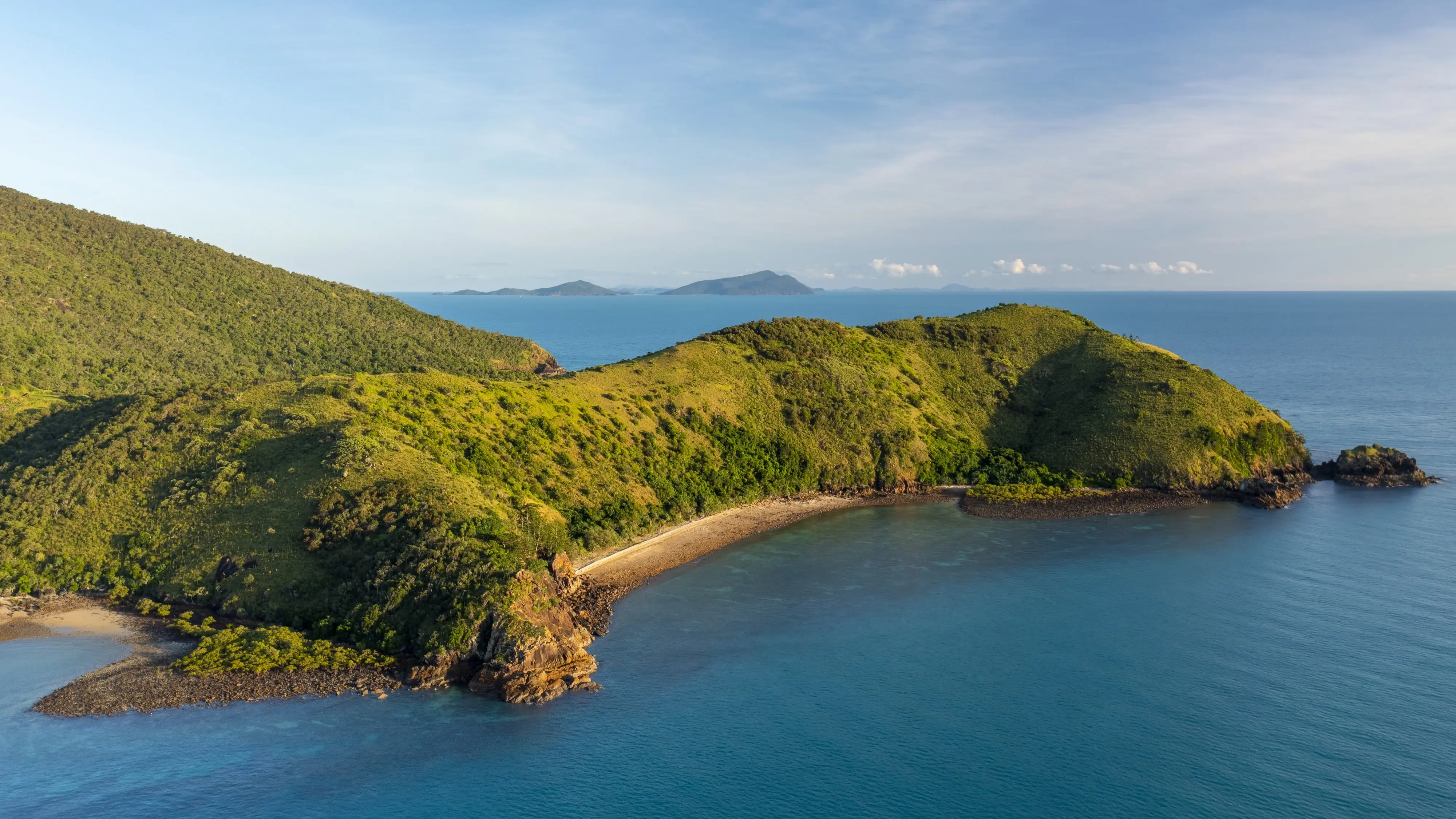 Aerial shot of hilly Keswick Island covered in greenery and surrounded by blue water. Image credit: Tourism and Events Queensland