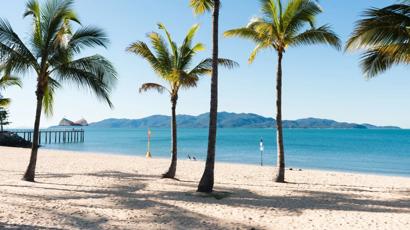 The Strand beach, Townsville, white sand and palm trees in the foreground, ocean, jetty and Magnetic Island in the background. Image credit: Shutterstock