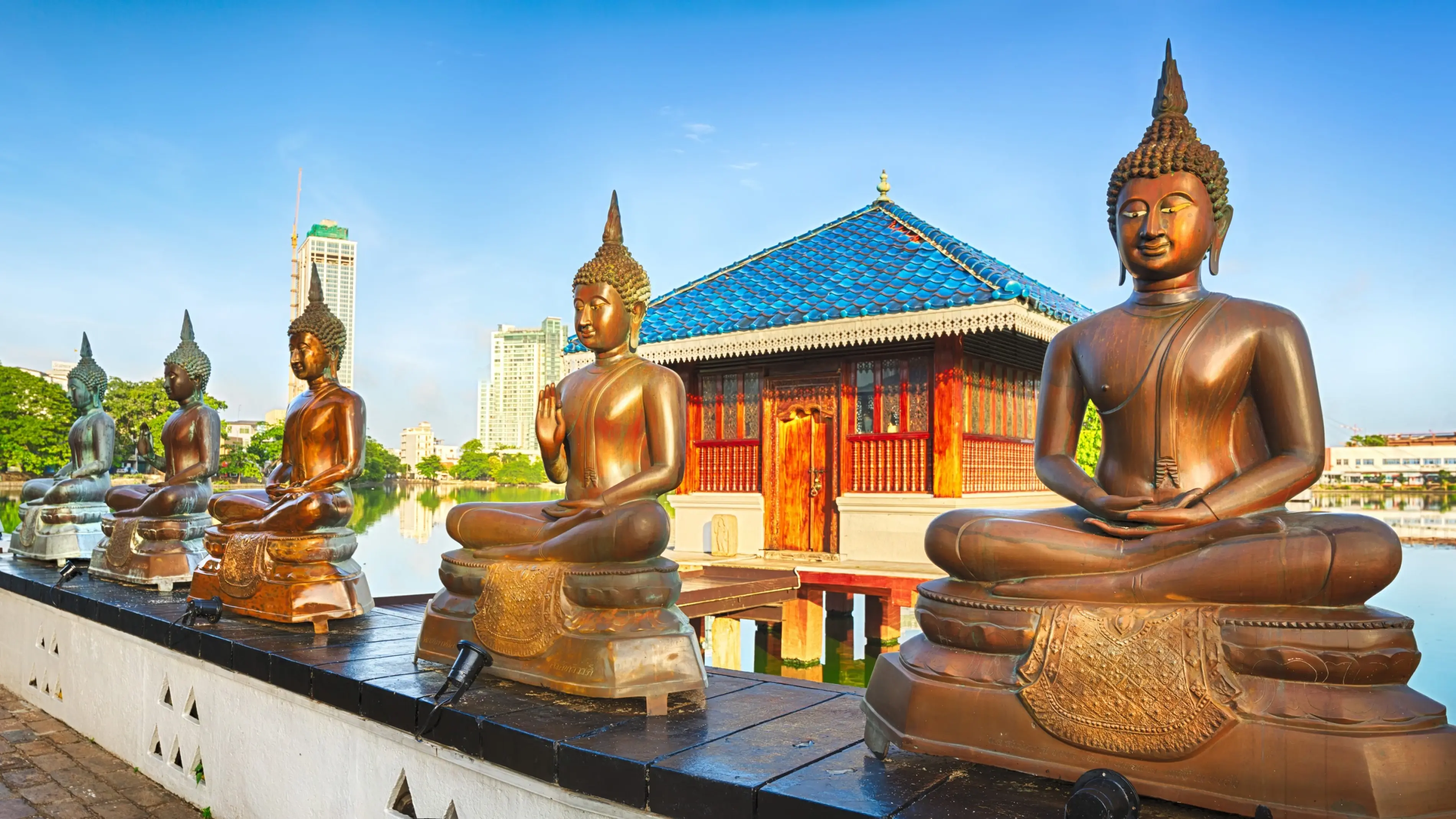 Row of Buddha statues at the entrance of Seema Malaka temple, with Beira Lake and Colombo skyline in the background. Image credit: stock.adobe.com