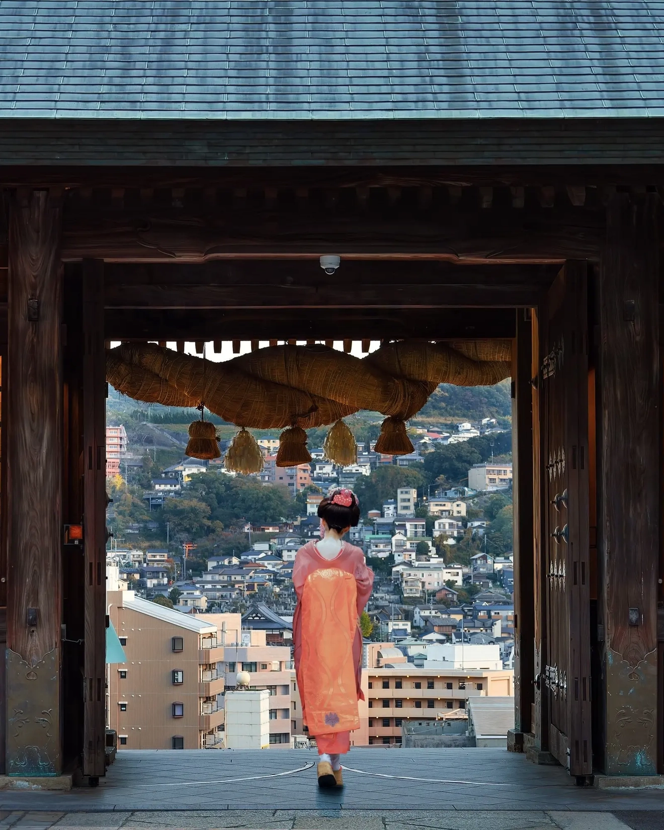 長崎市の建物を背景に、諏訪神社の入り口に立つ着物姿の女性。画像クレジット：stock.adobe.com